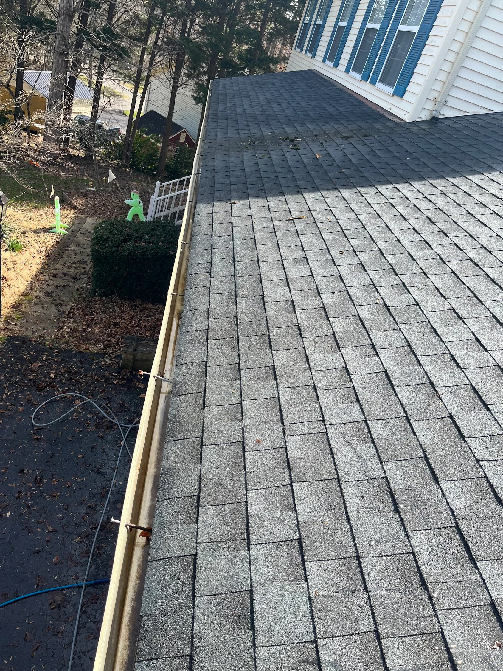 Clean gray architectural shingle roof with white gutters on residential home in wooded setting