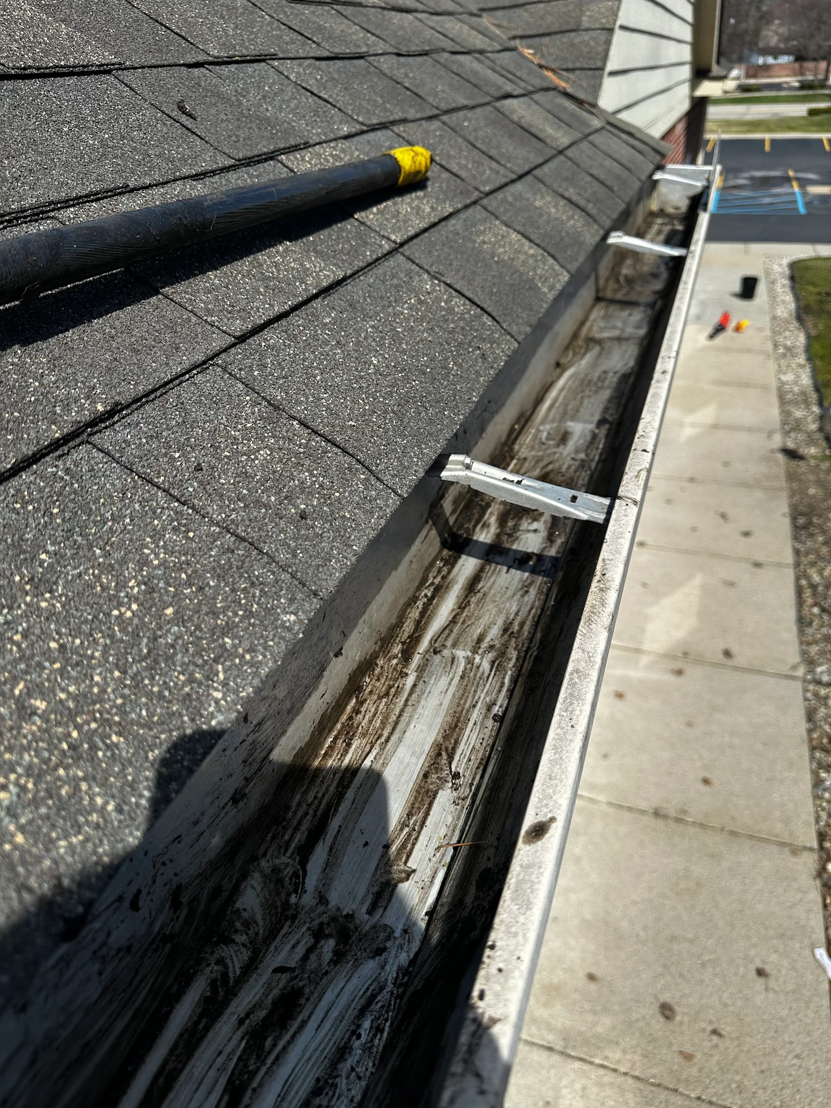 Close-up of gutter cleaning with black debris removal tool and aluminum gutter guard installation
