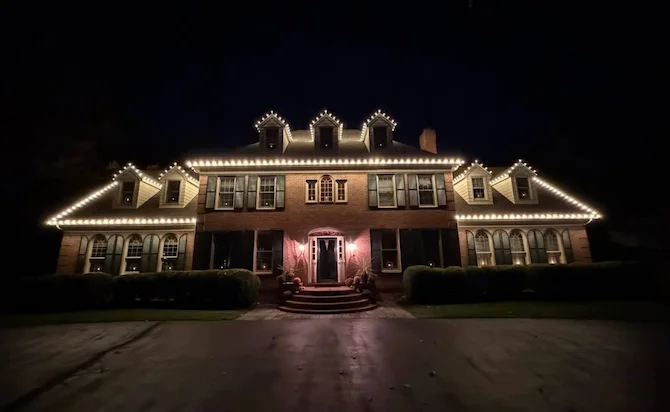 Brick colonial home with warm LED accent lighting along roofline and facade at night