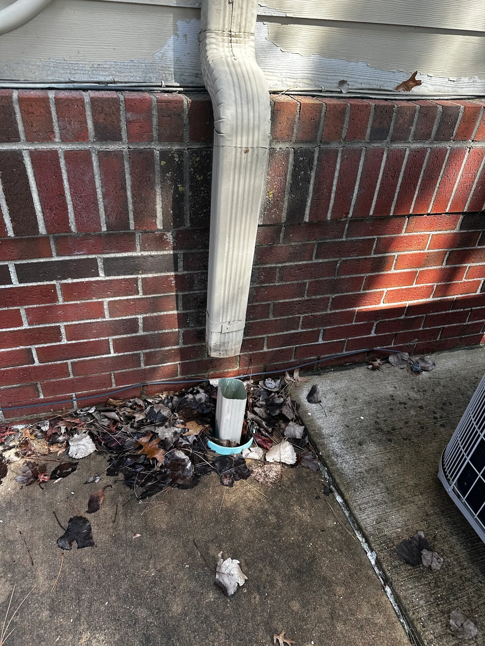 White downspout cleaned against red brick foundation with debris removal