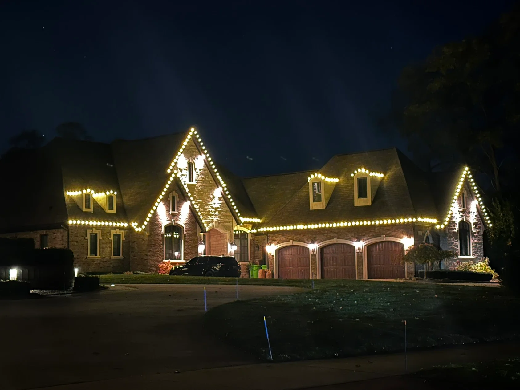 Brick home at night with warm white LED lights outlining roofline and gables