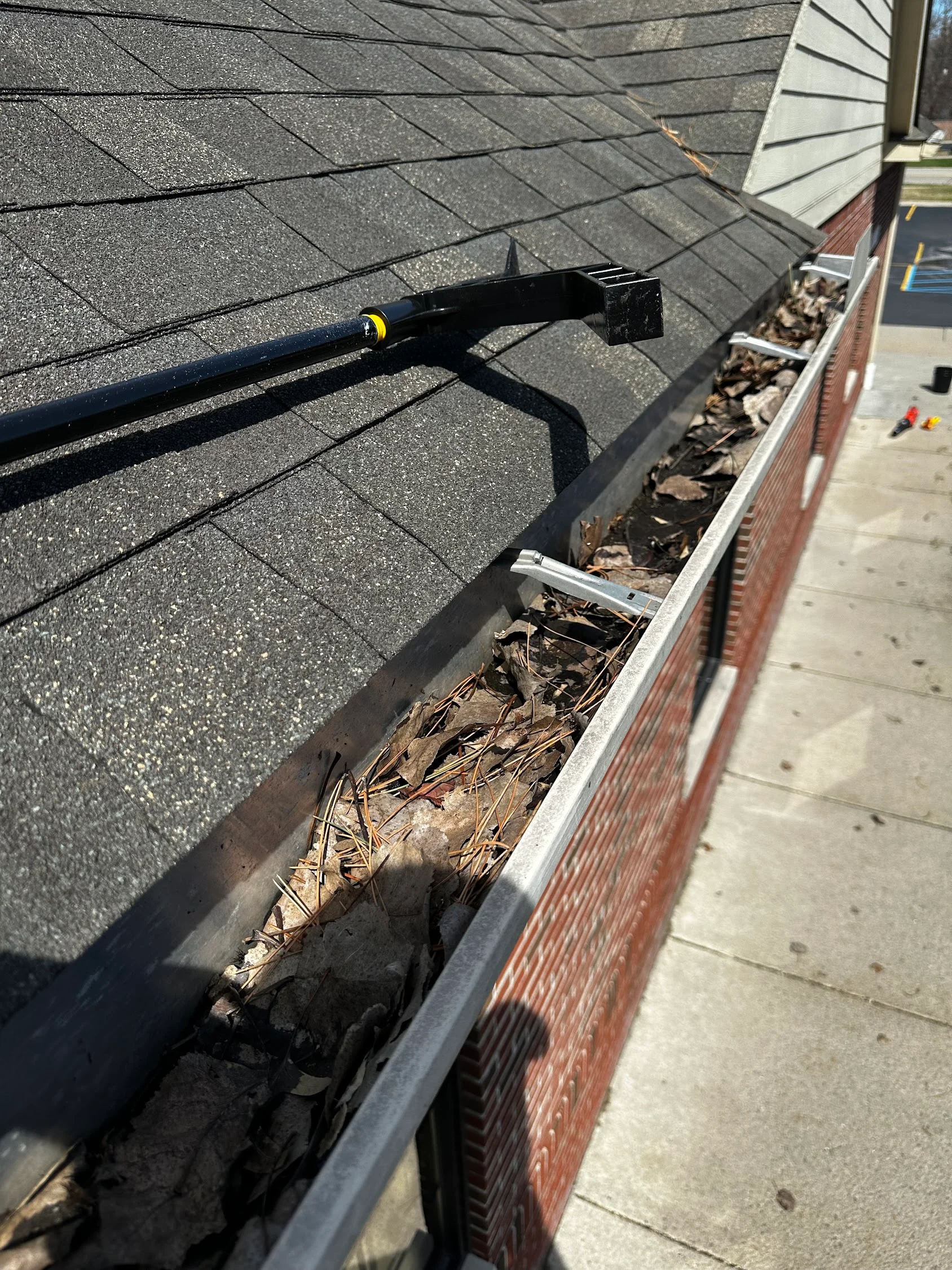 Black gutter being cleaned with debris removal tool on brick home with asphalt roof