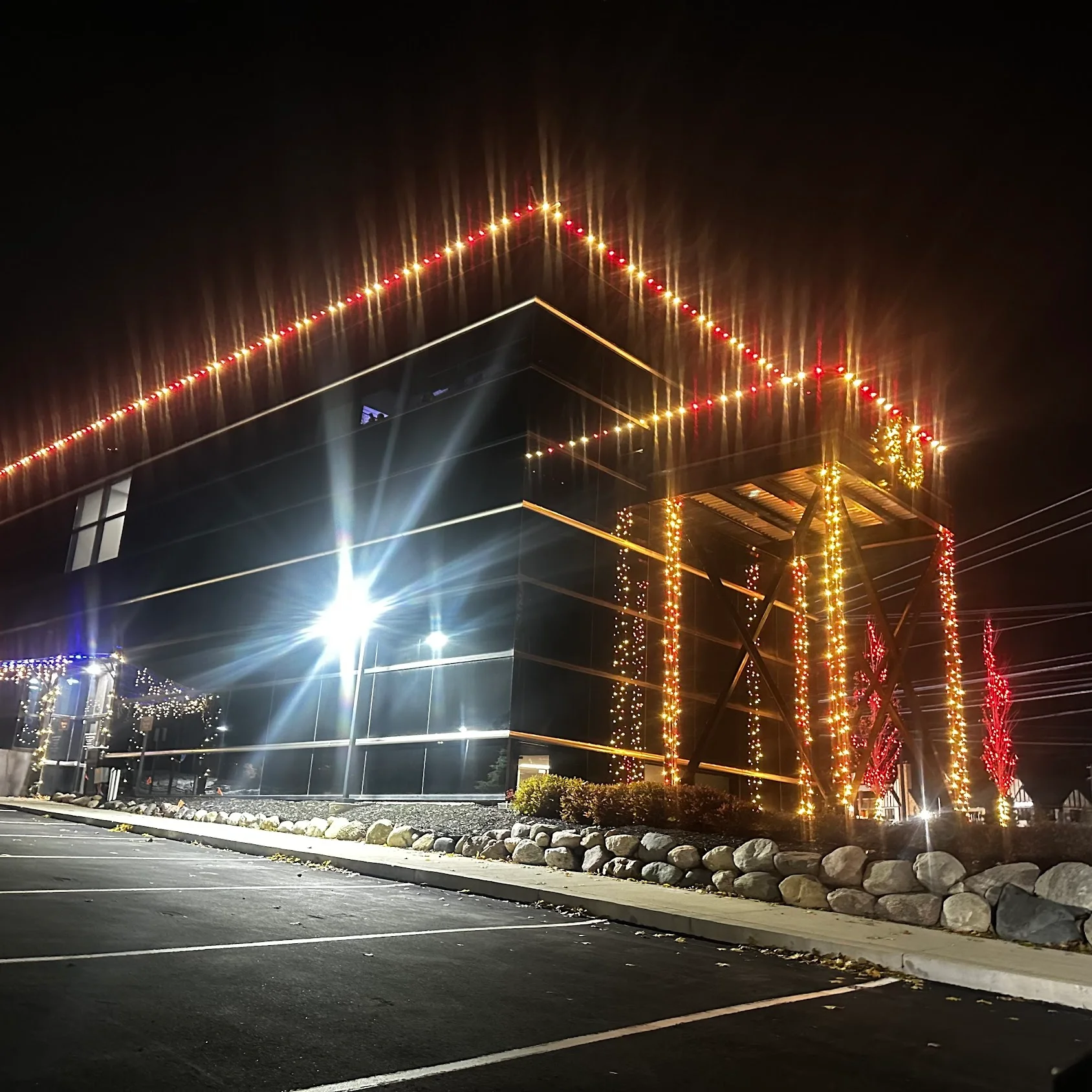 Modern commercial building at night with red and gold LED lights outlining roofline and columns