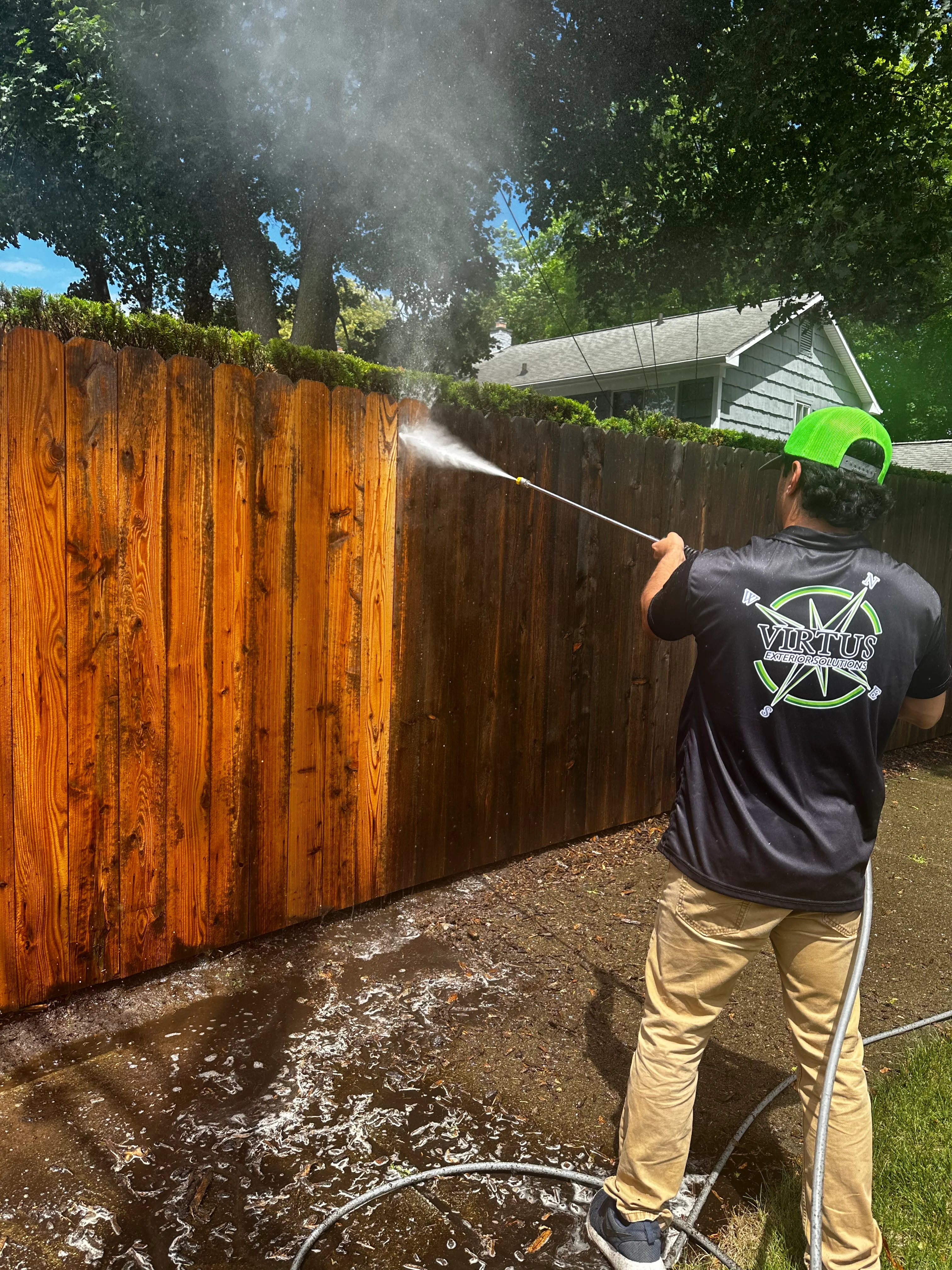 Technician pressure washing wooden fence with high-pressure spray equipment
