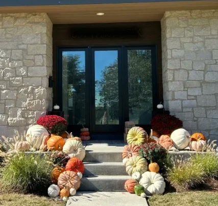 Colorful pumpkins, gourds, and mums arranged along stone steps leading to a home's entrance